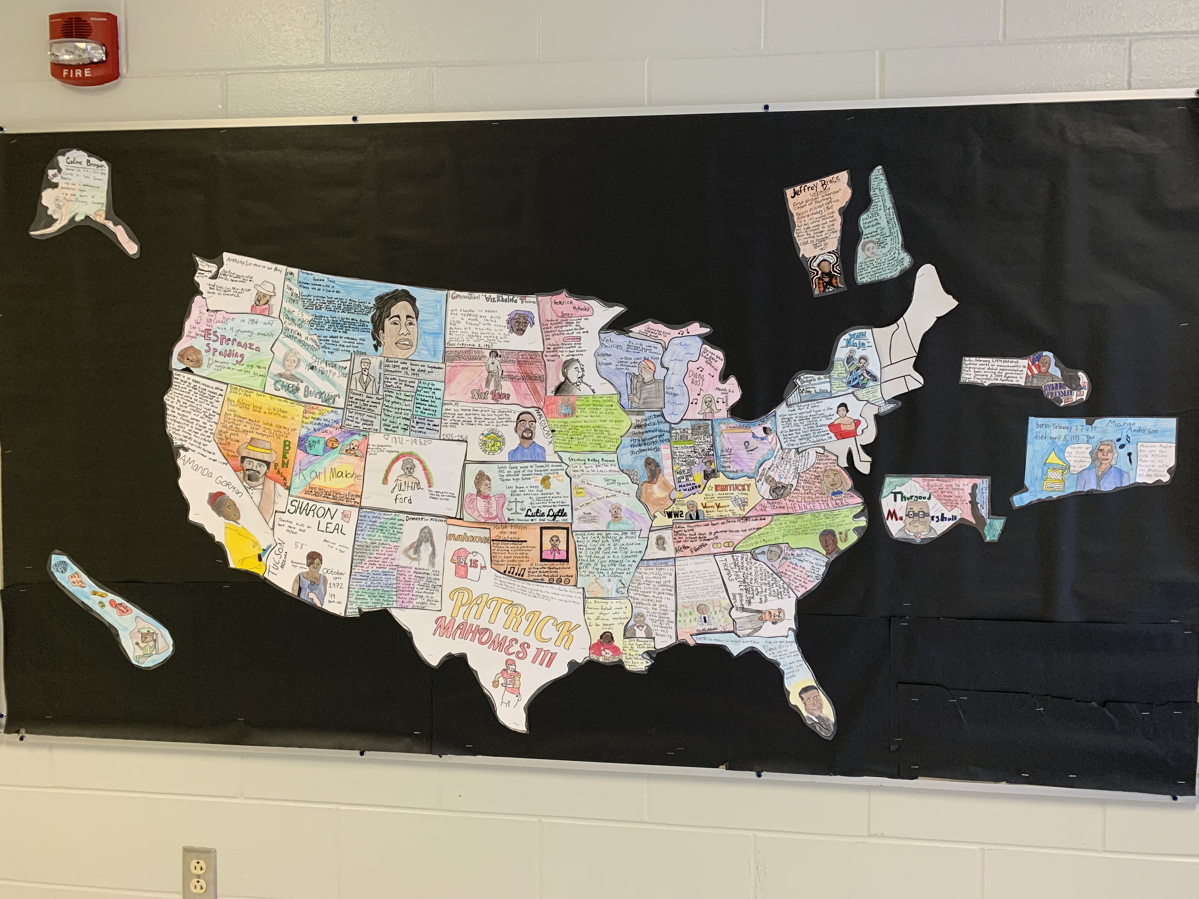 A large bulletin board with a colorful U.S. map, each state filled with unique drawings or collages. Alaska and Hawaii are in the bottom left. The background is black, with a red fire alarm above the map